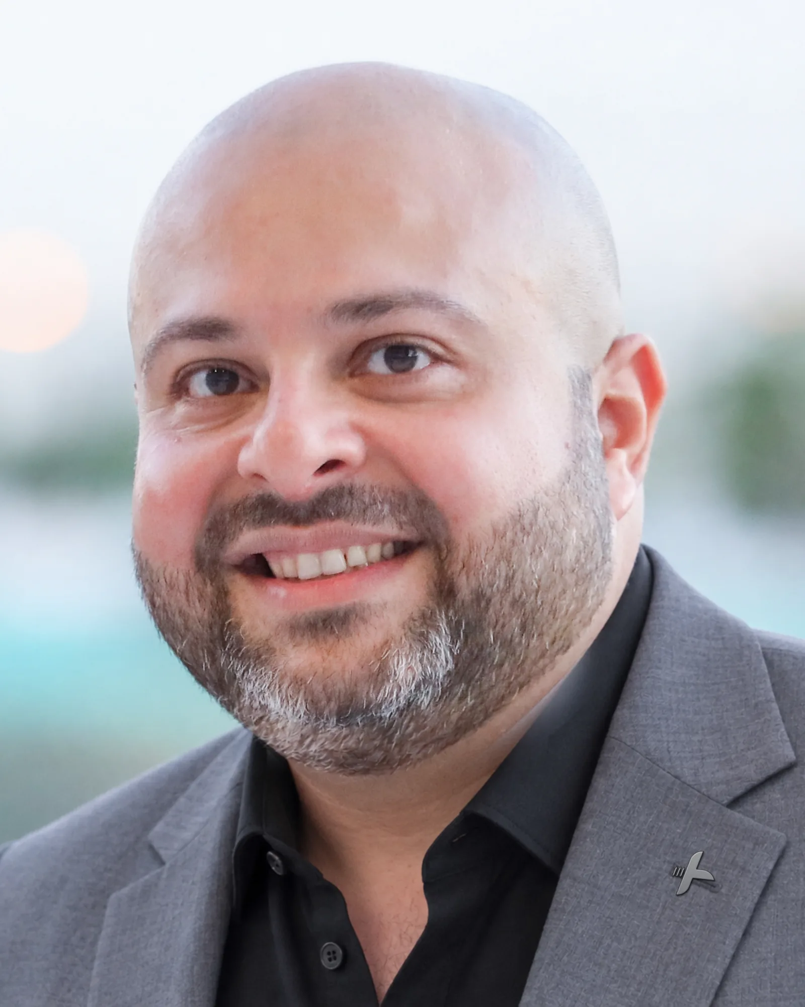Antoni Gerges, smiling, in a grey suit and an open-collar black shirt