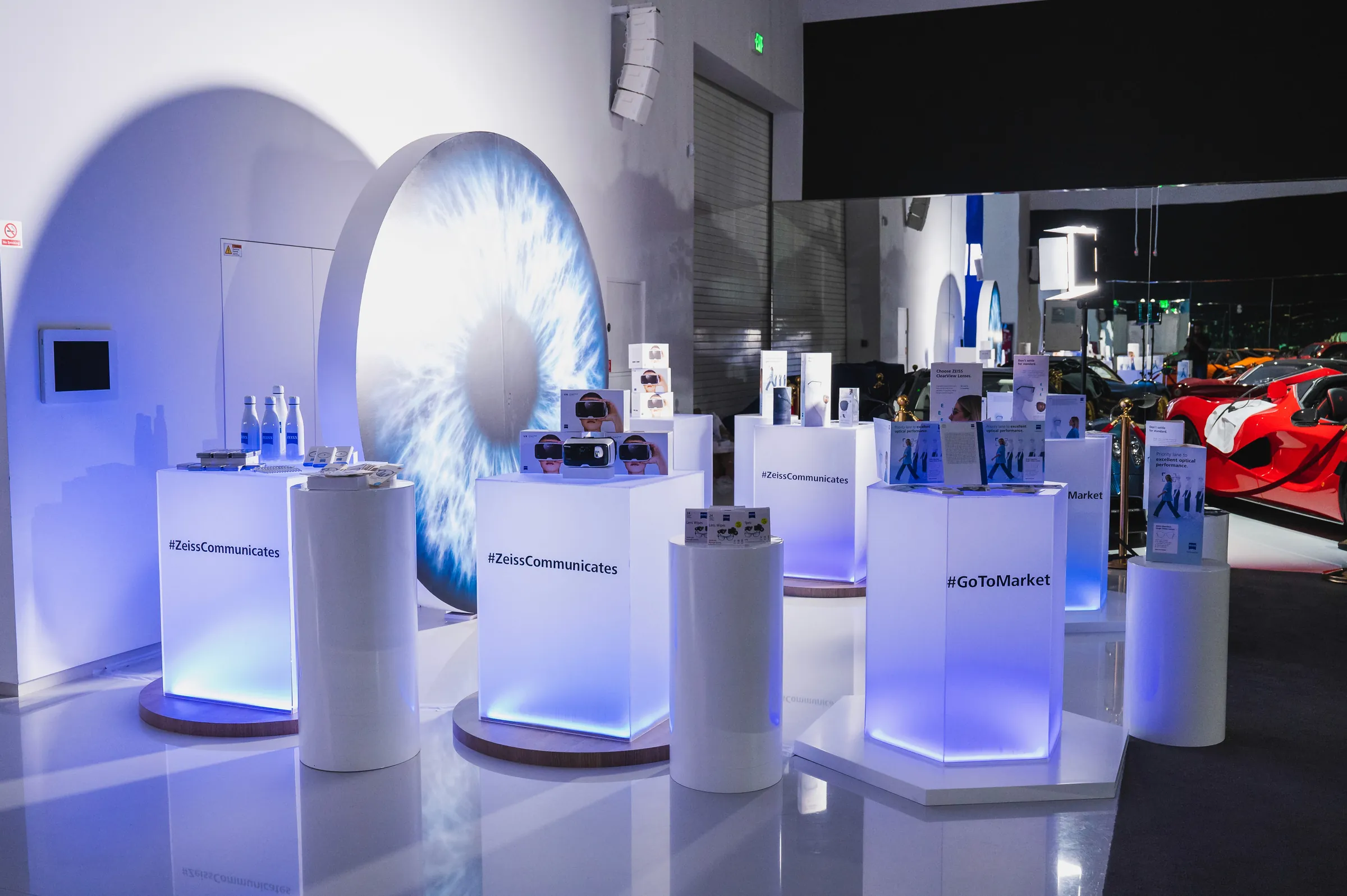 The ZEISS launch wall as built: a great eye on a white wall, lit plinths in front of it