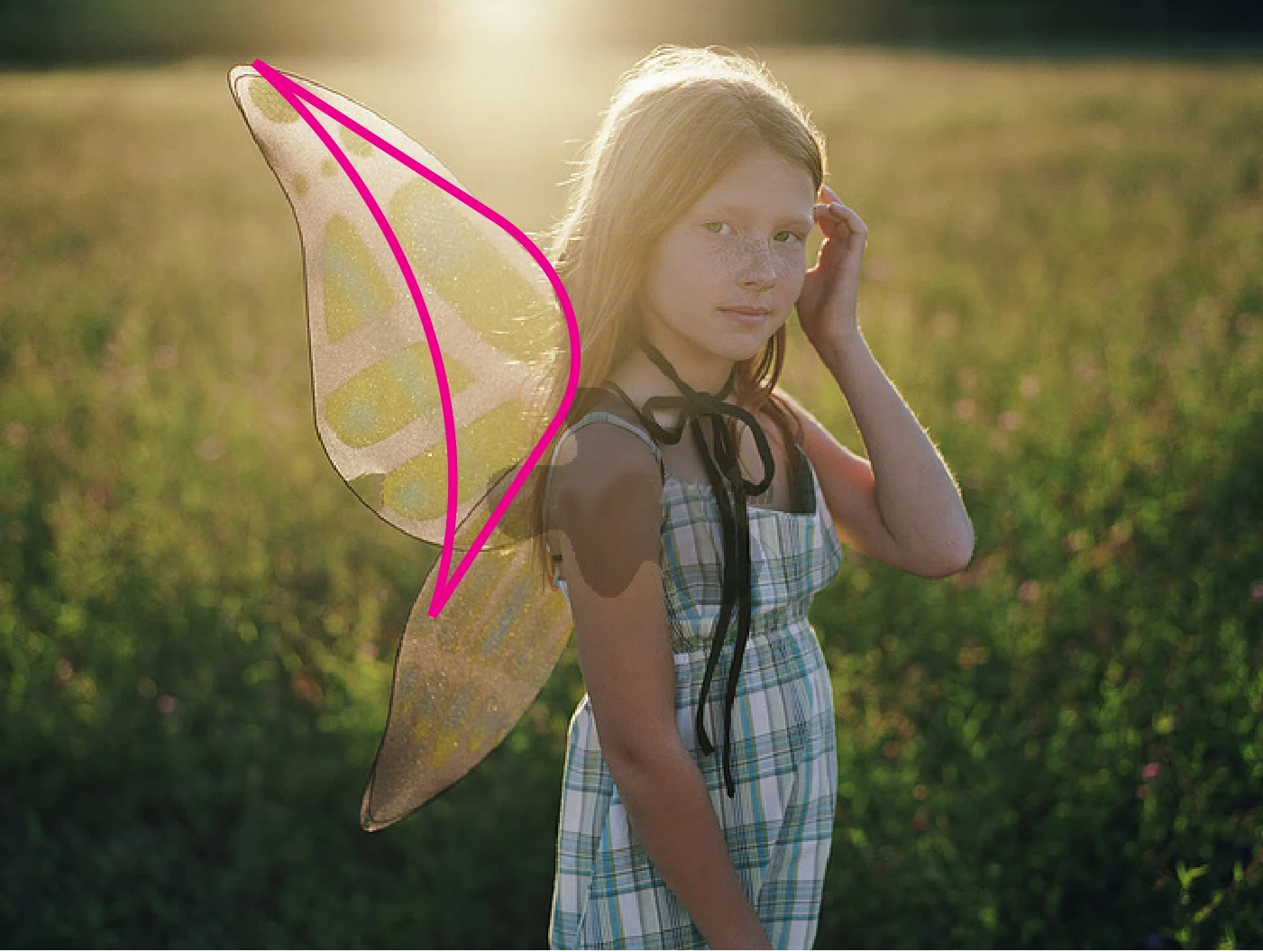 A girl in a field wearing clear wings, one wing traced in magenta.