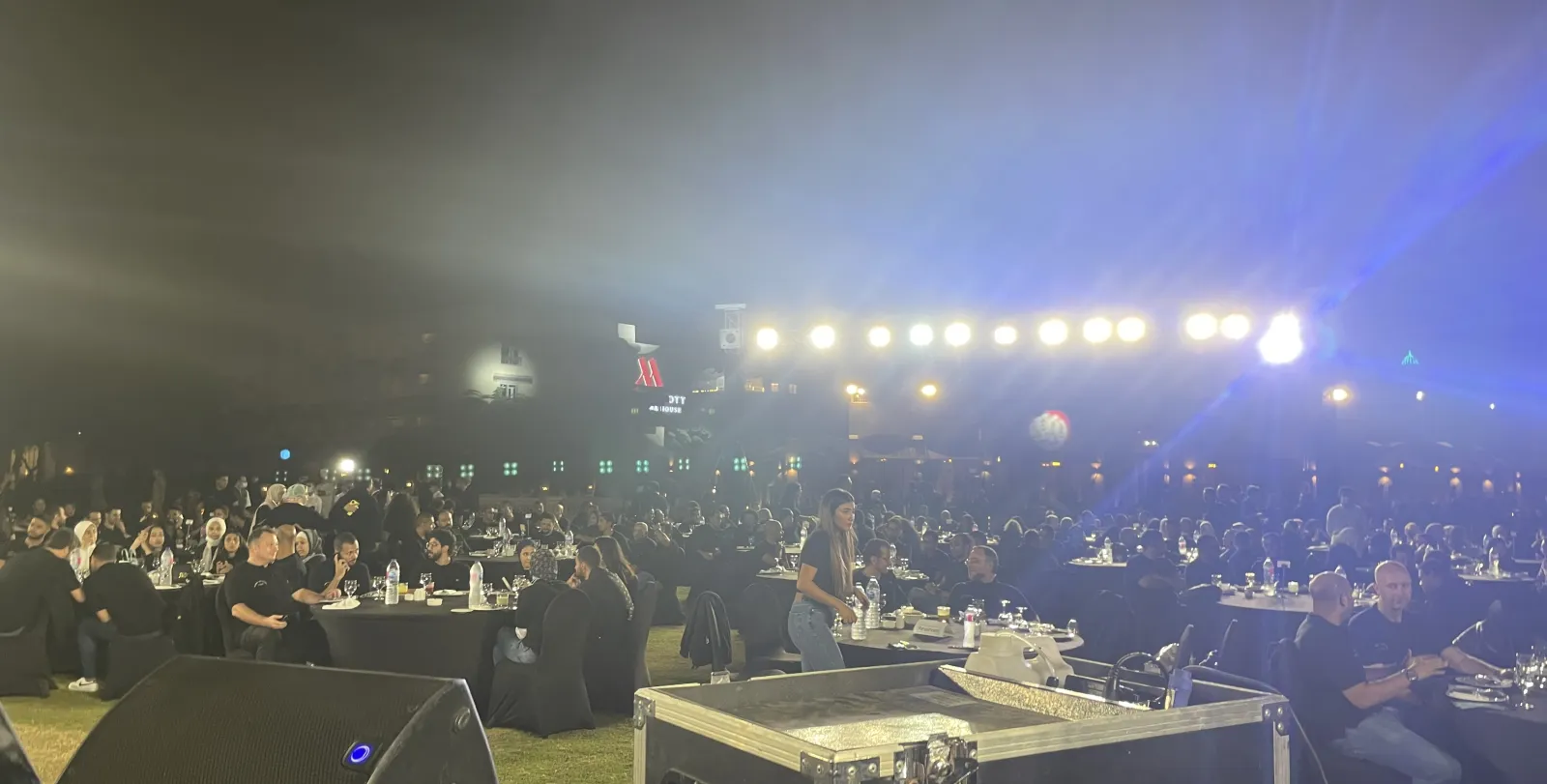 The night of the event: guests at round tables on the lawn under a row of stage lights.