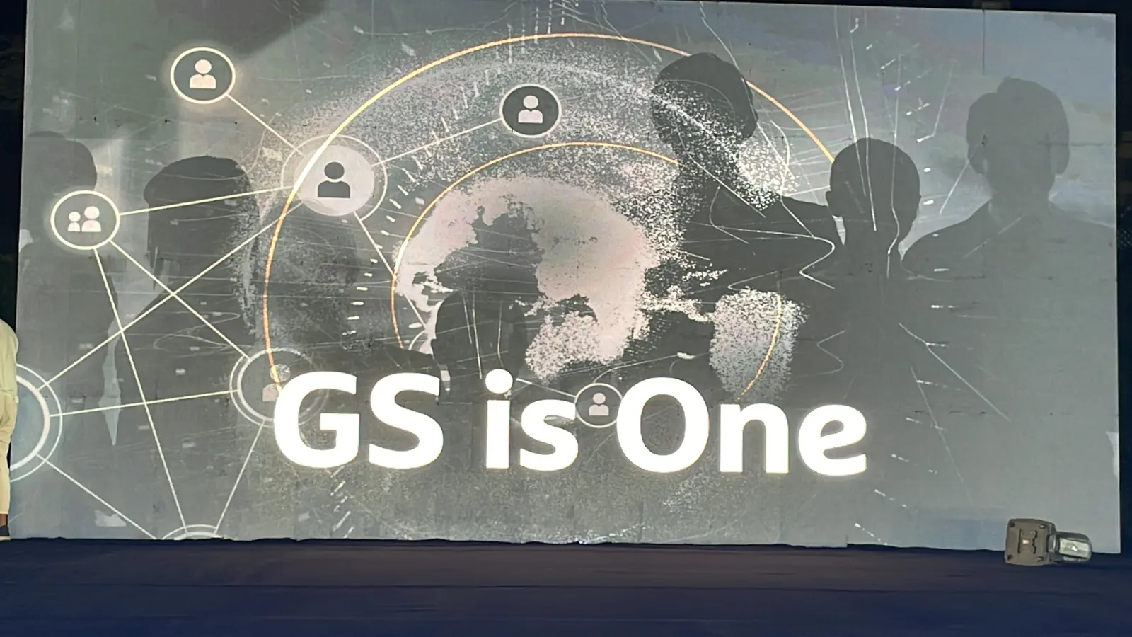 The LED wall at night showing a globe of connected people and the words GS is One.