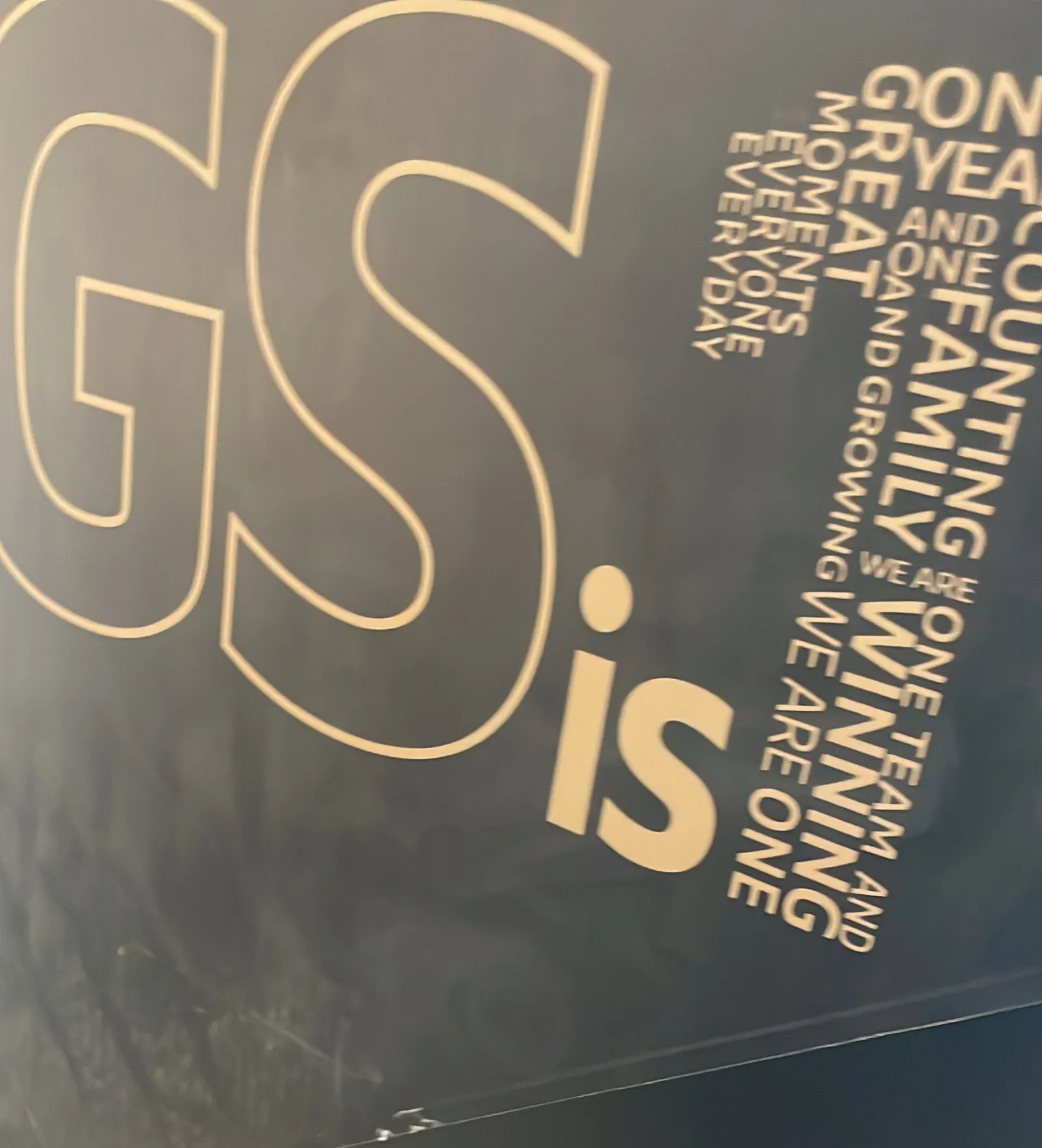 A black totem lying on the paving before it was stood up: the letters GS and a stack of words in gold.