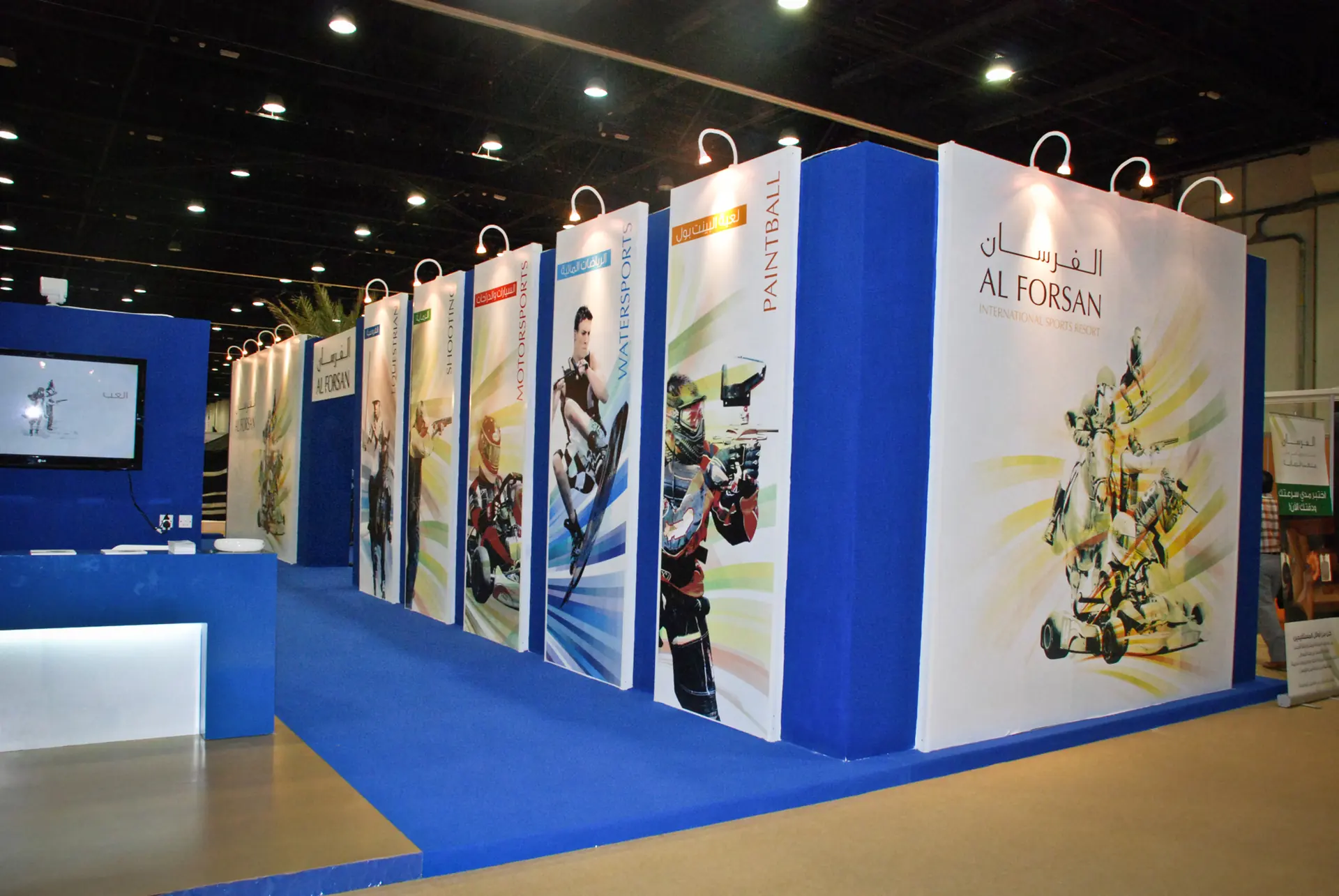 Photograph: the exhibition stand, a row of tall banners, one for each sport centre, each named in its own colour, beside a wall with the two names of the resort