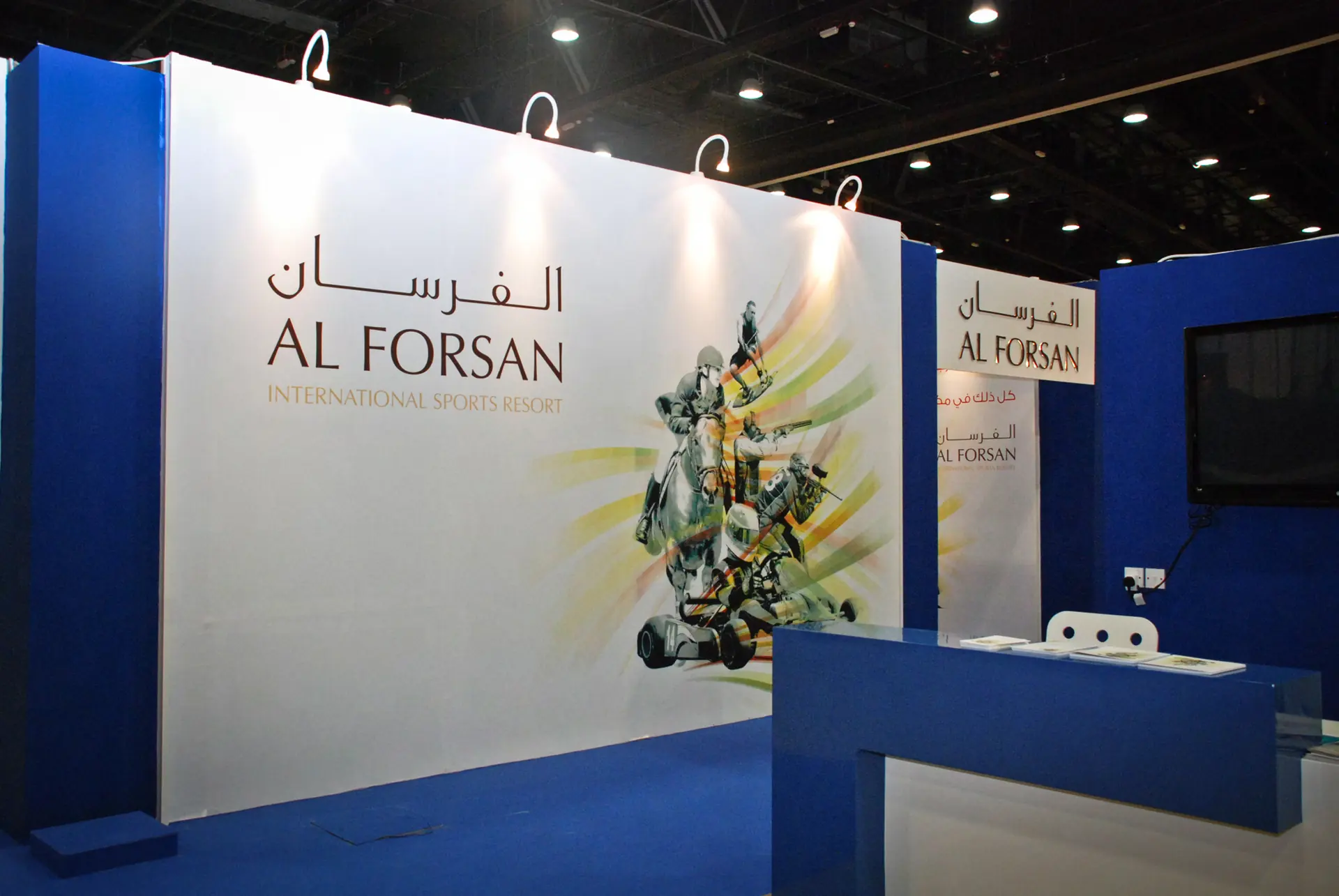 Photograph: a white wall of the stand with the two names of the resort and the five sports drawn in green and gold strokes