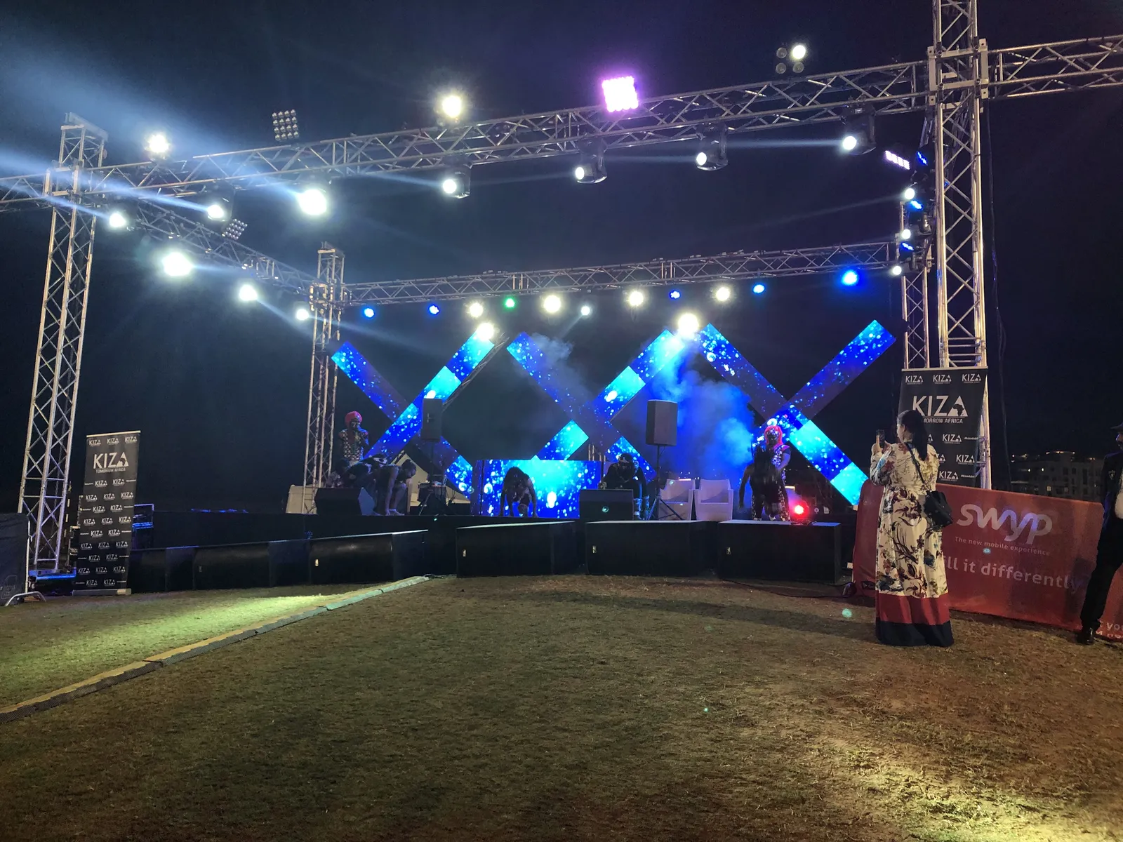 The stage with its three lit X’s on the first night, KIZA on stage, seen from the lawn