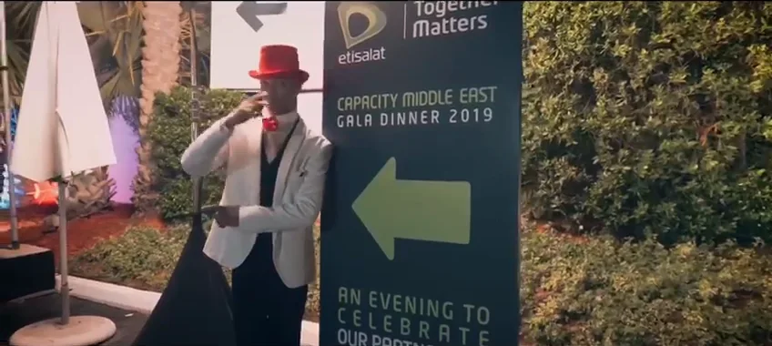 A frame of the event film: a performer in a red hat beside the directional sign, Capacity Middle East Gala Dinner 2019, An evening to celebrate our partnership